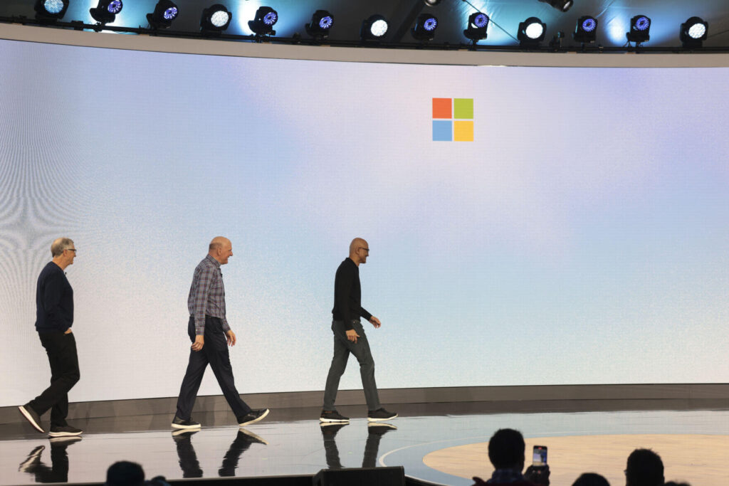 Bill Gates, Steve Ballmer, and Satya Nadella walking on stage together during a Microsoft event, with the Microsoft logo in the background.